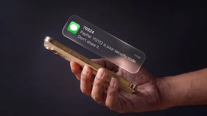 A hand holds an iPhone as a Messages notification floats above it, reading: “PayPal: 112112 is your security code. Don’t share it.”